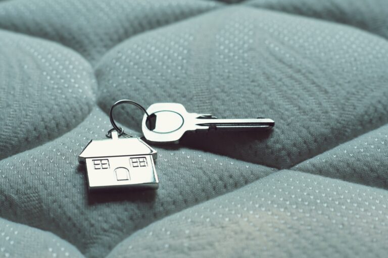 Home key with house keychain on bed, property concept